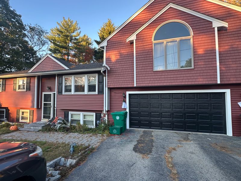 Black raised-panel double garage door on red-sided home with arched window