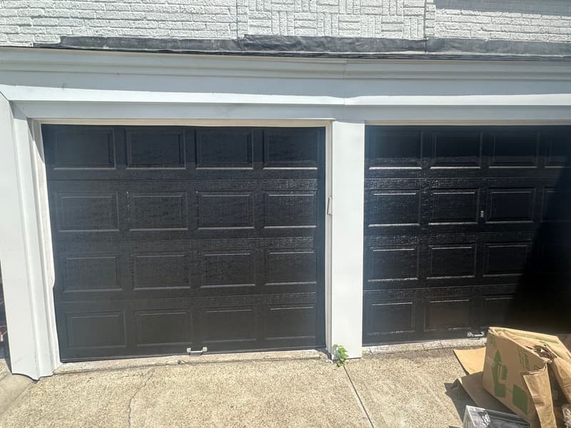 Black dual raised-panel garage doors on gray stone-faced home
